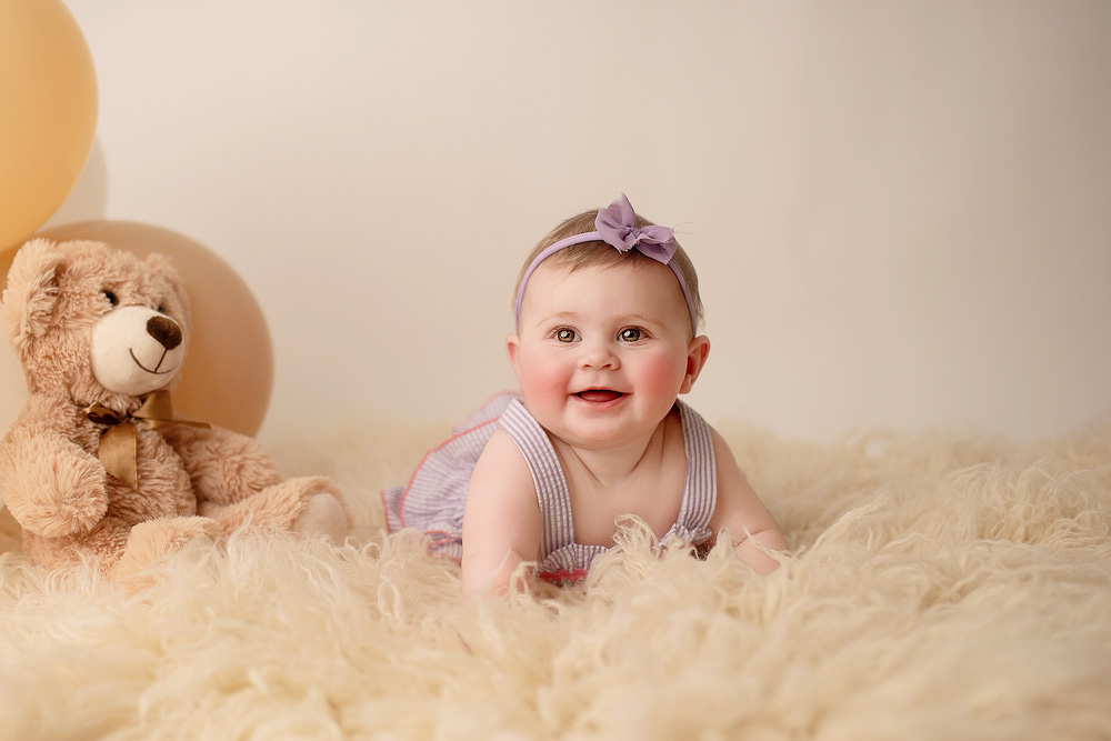 Smiling baby at her Five-month milestone photoshoot, capturing tummy time, wearing a
purple outfit and matching bow headband, in Houston, TX